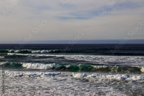 Foamy aqua colored waves hitting the coast with patches of blue peeking through a mostly cloudy sky