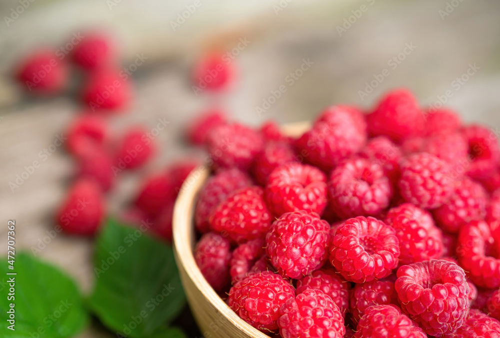 Fresh ripe red raspberries with leaves in a bowl on rustic old wooden table. Healthy organic food, summer vitamins, BIO viands, natural background. Copy space for your advertising text message.