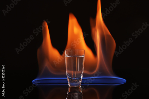 Vodka in shot glass and flame on black background