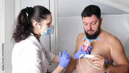 man patient with ECG cardiogram of heart, doctor cardiologist attaches sensors, examining and monitoring using holter equipment device for 24 hours daily monitoring of electrocardiogram, recorder photo