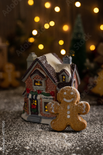 Gingerbread man cookie near toy Candy house with snow and lights. Vertical with copy space