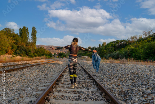Rear view of woman stretching out her arms on railroad tracks. A woman waiting for a train passenger. A woman longing for a vacation.