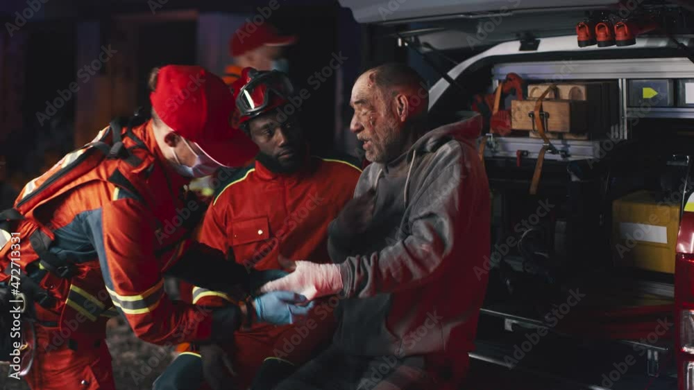 Multiracial emergency service workers putting blanket and bandaged injured hand of aged man during interrogation after accident at night Multiracial emergency service workers putting blanket and bandaged injured hand of aged man during interrogation after accident at night