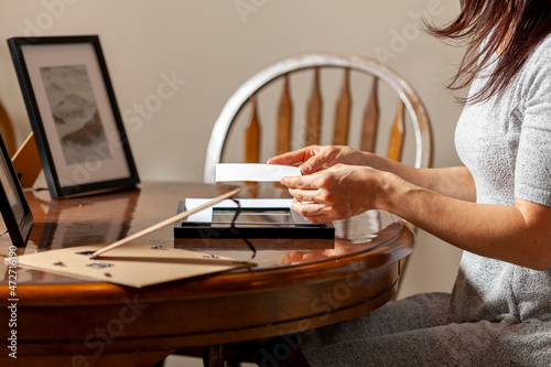 фотографія A young caucasian woman is placing a printed photograph into a picture frame with kickstand