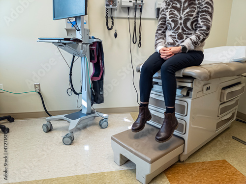 Inside of an  exam room with a bed, some medical devices, a computer. A woman is anxiously waiting for the doctor. Generic image for health care industry, disease, patient and doctor.