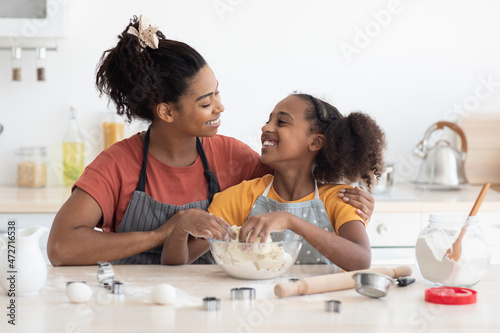 Cute smiling african american mother and daughter cuddling while baking
