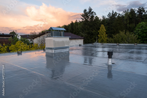 Flat roof covered with bitumen membrane and silver lacquer with chimney on a private house. Reflections after rain photo