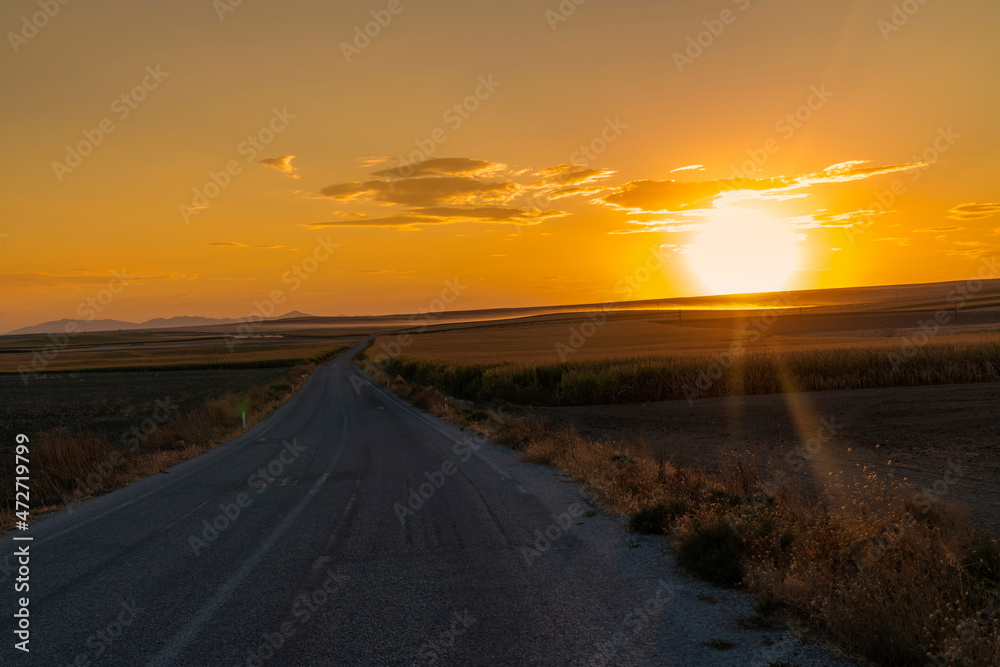 Asphalt road between fields and sunset in the background. Konya, Turkey.