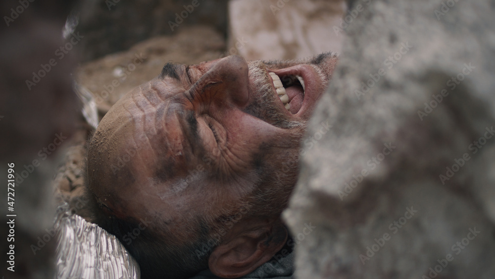 Naklejka premium High angle of aged male survivor screaming for help while lying under remains of destroyed building after earthquake