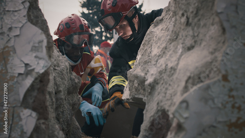 Black rescuer talking with colleague while sitting near rubble and rescuing survivors after disaster