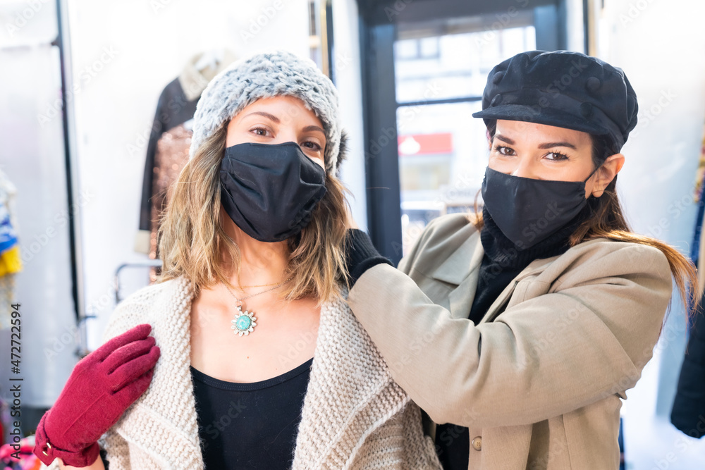 Employee with a mask in a clothing store trying on a client a jewel, working with security measures in the coronavirus pandemic, covid-19 Employee with a mask in a clothing store trying on a client a jewel, working with security measures in the coronavirus pandemic, covid-19