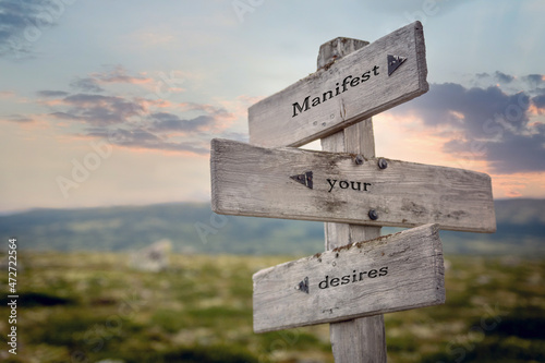 manifest your desires text quote on wooden signpost outdoors in nature.