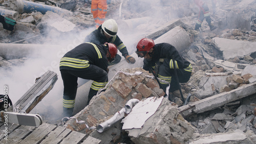 Foto Men in protective uniforms and hardhats removing pieces of broken building durin