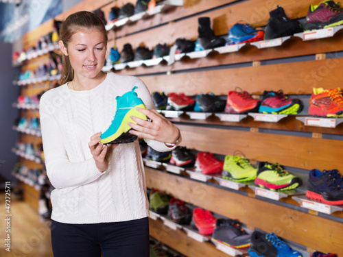 Young slender girl in a sports shop chooses her clothes and shoes for training