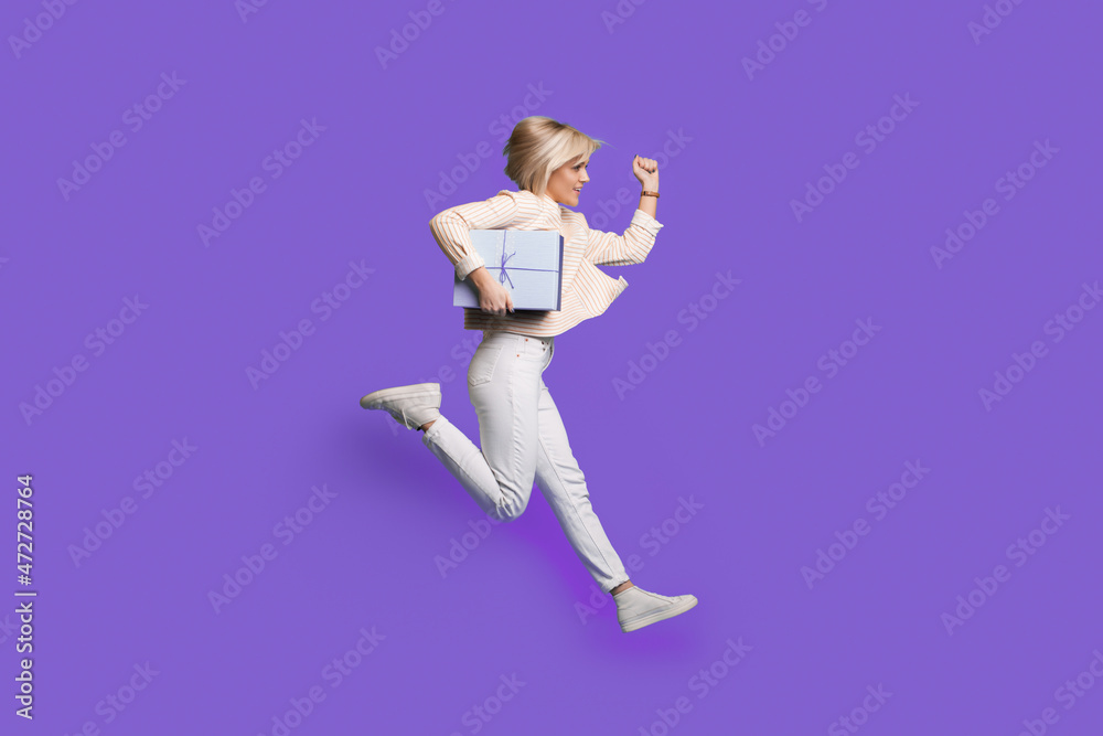Full body profile photo of a woman run holding gift wear sweatshirt and sneakers isolated over purple background. Happy birthday holiday. Full body profile photo of a woman run holding gift wear sweatshirt and sneakers isolated over purple background. Happy birthday holiday.