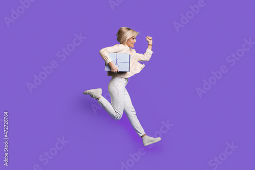 Full body profile photo of a woman run holding gift wear sweatshirt and sneakers isolated over purple background. Happy birthday holiday.