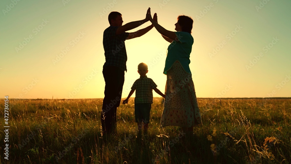 Happy family dreams of their own house in the park in the summer in the sun. Parents take care of children. Children, mom and dad, together building a house with their own hands, silhouette at sunset.