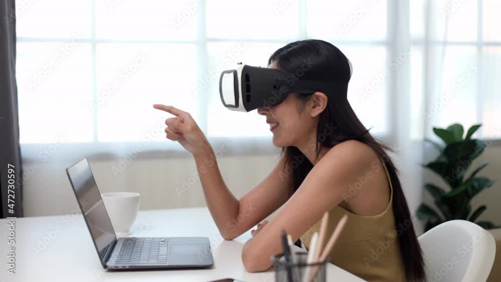 Young asian woman put on vr glasses into virtual simulated world metaverse chatting conference online sitting in living room at home. Business Woman Meeting on social media Learning from home. Young asian woman put on vr glasses into virtual simulated world metaverse chatting conference online sitting in living room at home. Business Woman Meeting on social media Learning from home.