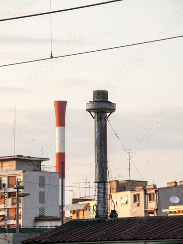 individual metal chinmey in the center of belgrade, serbia, with a blurred industrial red and white chimney in background, taken during a sunny afternoon, used for industry and energy production photo