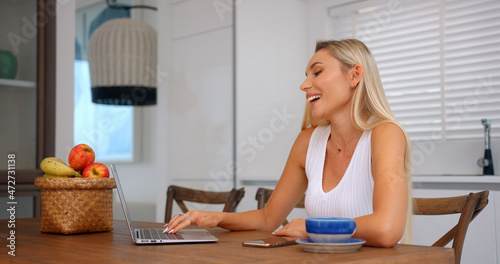 Freelancer woman sittting at table in kitchen having online video conference with her colleagues 