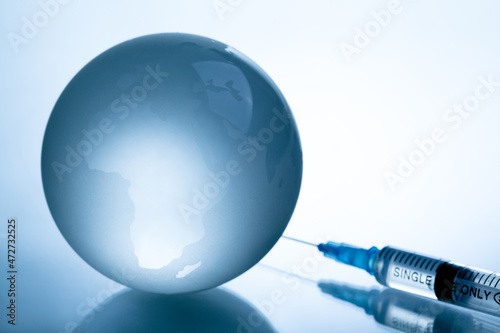 Medical syringe with a needle and a bollte with vaccine on world map.