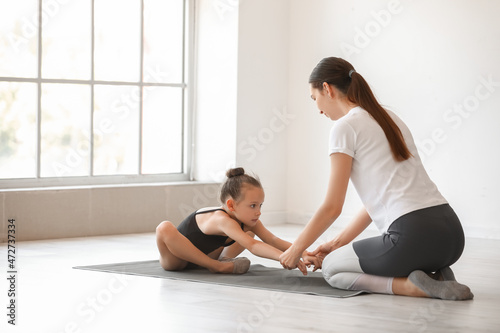 Coach helping little girl to do gymnastics in gym