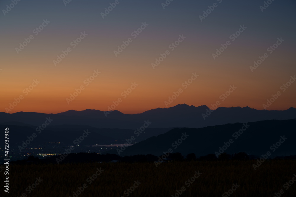 遠くに北アルプスのシルエットが浮かぶ山村の夕景