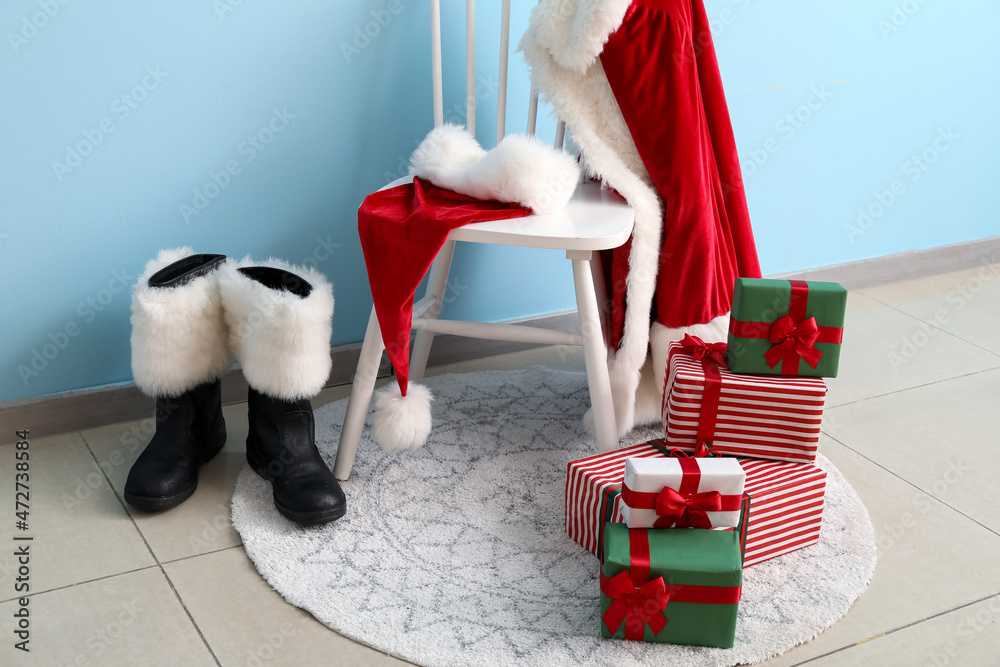 Obraz premium Chair with Santa costume, boots and Christmas gifts near color wall