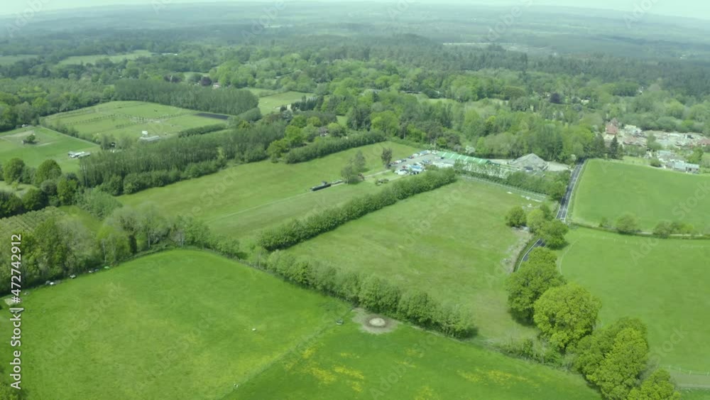Aerial view above green clean farm meadow patchwork countryside landscape tilting up into the distance Aerial view above green clean farm meadow patchwork countryside landscape tilting up into the distance