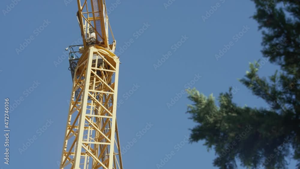 Top view of a tall yellow crane with a tree in the shot, on a sunny and windy day Top view of a tall yellow crane with a tree in the shot, on a sunny and windy day