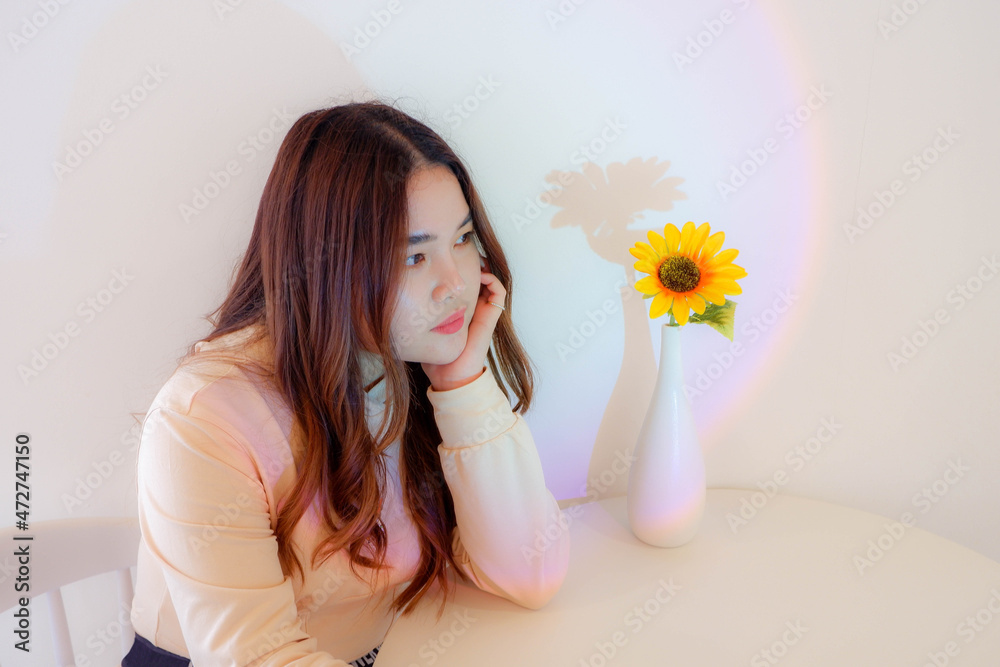 A young woman sitting alone with a background of flowers and lights. A young woman sitting alone with a background of flowers and lights.