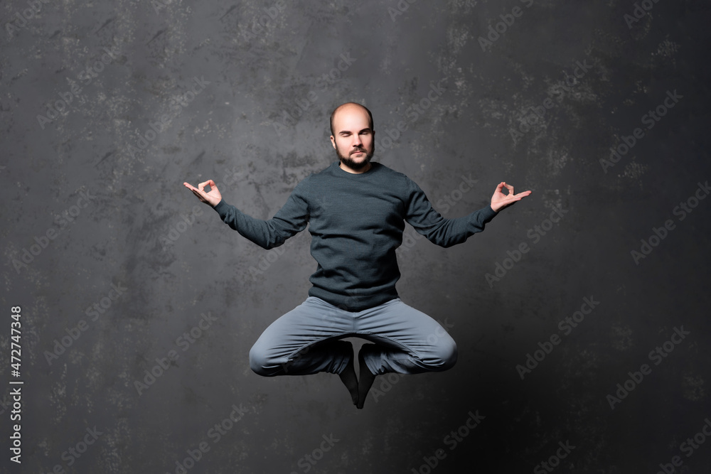 Man in meditation in flight, alone at home, peaceful calm guy practicing yoga in lotus pose indoors, holding hands in mudra, freedom and serenity concept