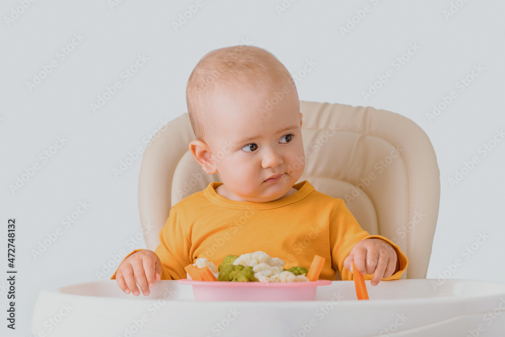 Toddler doesn't want to eat boiled vegetables. A baby sitting on a feeding chair does not want to eat boiled broccoli, cabbage and carrots Toddler doesn't want to eat boiled vegetables. A baby sitting on a feeding chair does not want to eat boiled broccoli, cabbage and carrots