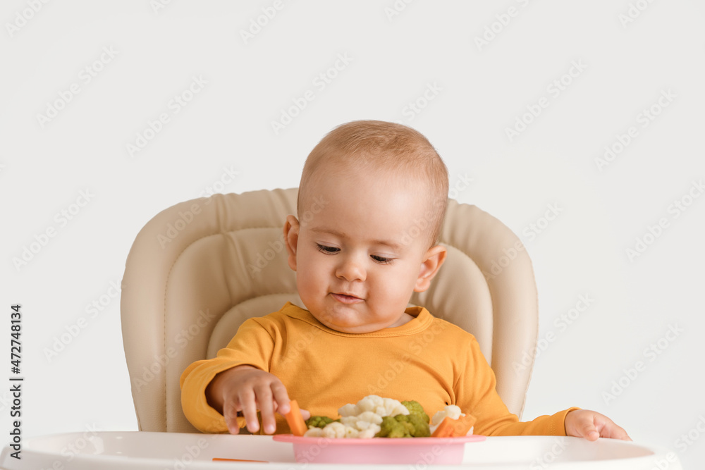 A baby eats boiled carrots and other vegetables while sitting on a feeding chair. Baby food in a vegan family A baby eats boiled carrots and other vegetables while sitting on a feeding chair. Baby food in a vegan family