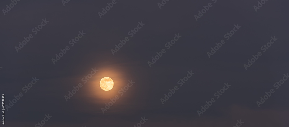 Rising full moon and light clouds against the backdrop of a twilight sky