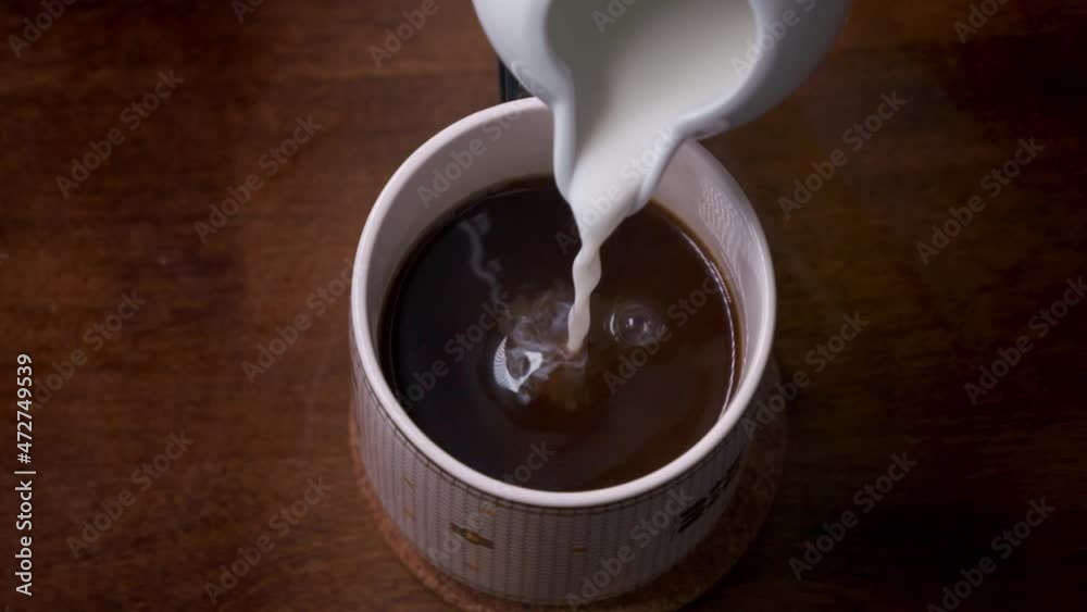 Super slow motion of cream splashing into a warm cup of coffee. The pour continues until a cloud of cream swirls to the surface amidst the dark brown roast. Super slow motion of cream splashing into a warm cup of coffee. The pour continues until a cloud of cream swirls to the surface amidst the dark brown roast.
