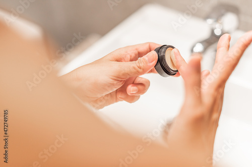 Hands of woman holding pot of anti-dark circles cream.