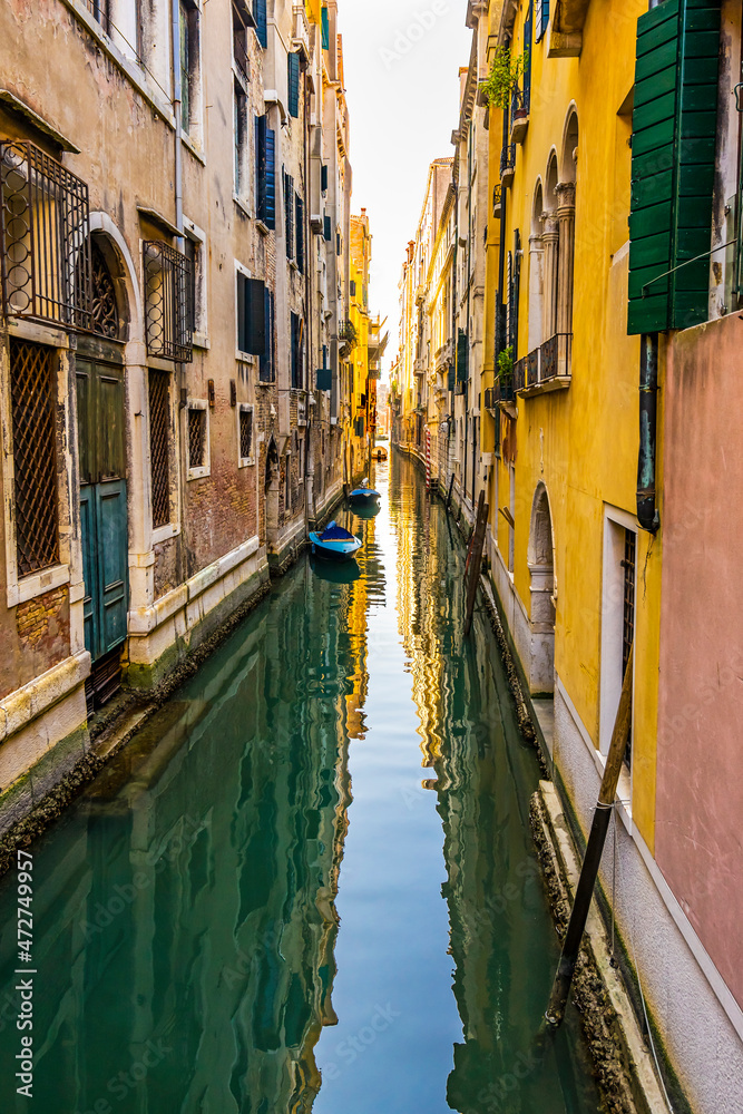 Colorful small canal and boats creating beautiful reflection in Venice, Italy.