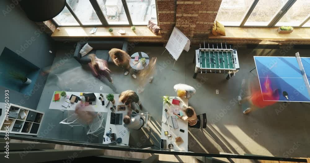 Zoom-in time lapse of creative youth working in modern business location during workday walking and talking and using laptops. People and job concept.