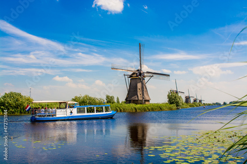Fotografia Canal tour boat and windmill in Unesco World Heritage Site, Kinderdijk, Holland, Netherlands