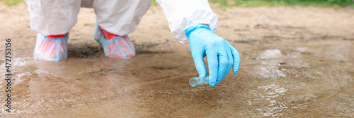 Scientist in protective suit collecting water in test tube from lake closeup