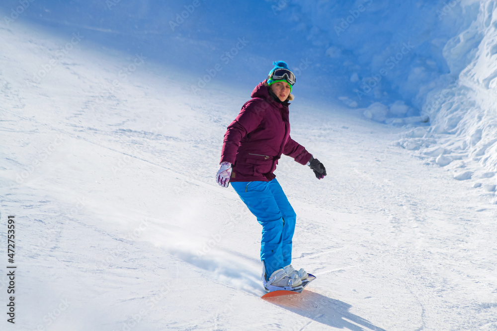 A young pretty girl slides down the slope on a snowboard. Lone snowboarder on the ski slope. Active recreation during the winter vacations.