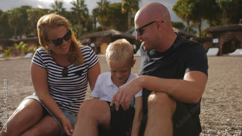 A friendly family with a young son are sitting together on the seashore and admiring the seascape. A happy family hugs on the seashore. A friendly family with a young son are sitting together on the seashore and admiring the seascape. A happy family hugs on the seashore.