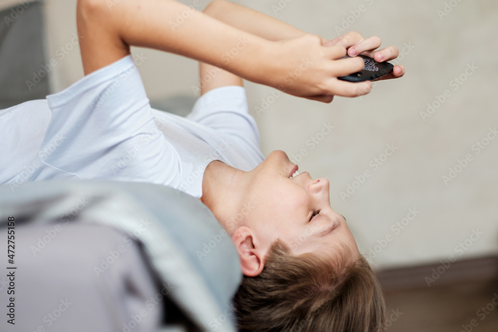 An 11-year-old teenager is lying on the bed with a phone in his hands. The problem of gadgets in children. An 11-year-old teenager is lying on the bed with a phone in his hands. The problem of gadgets in children.