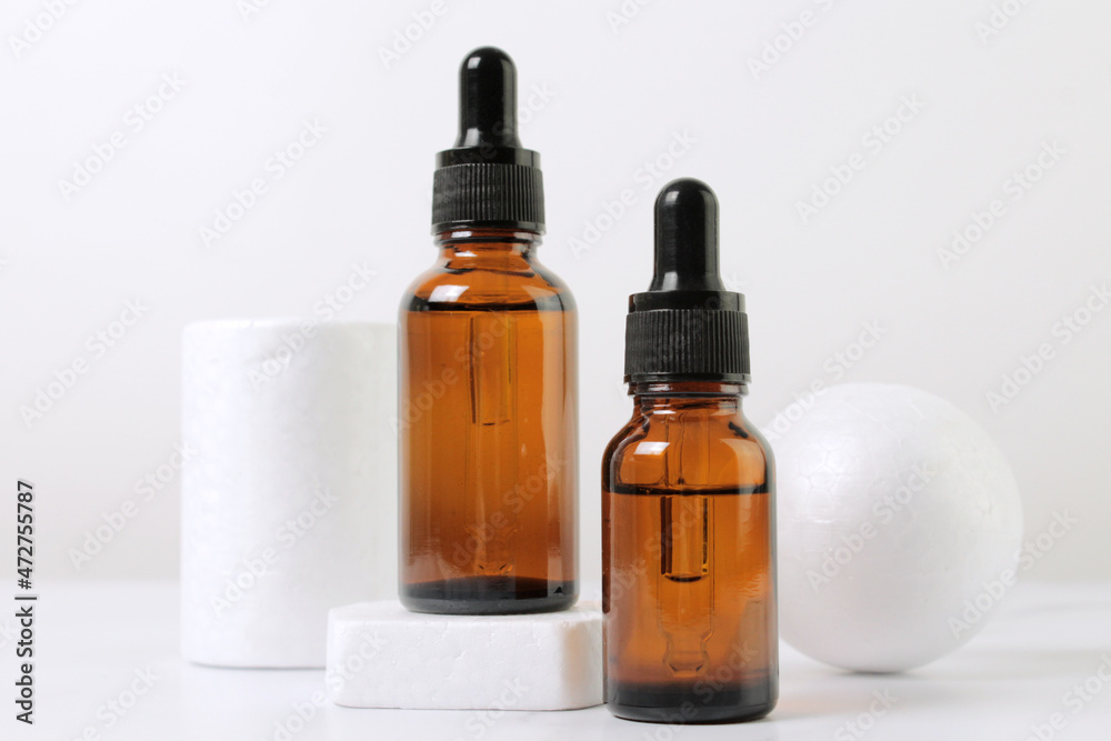 A mock-up of an empty glass dropper bottle made of brown glass stands on a white podium and a white background. Skin care serum, banner or template. The concept of a natural cosmetic product.Copyspace