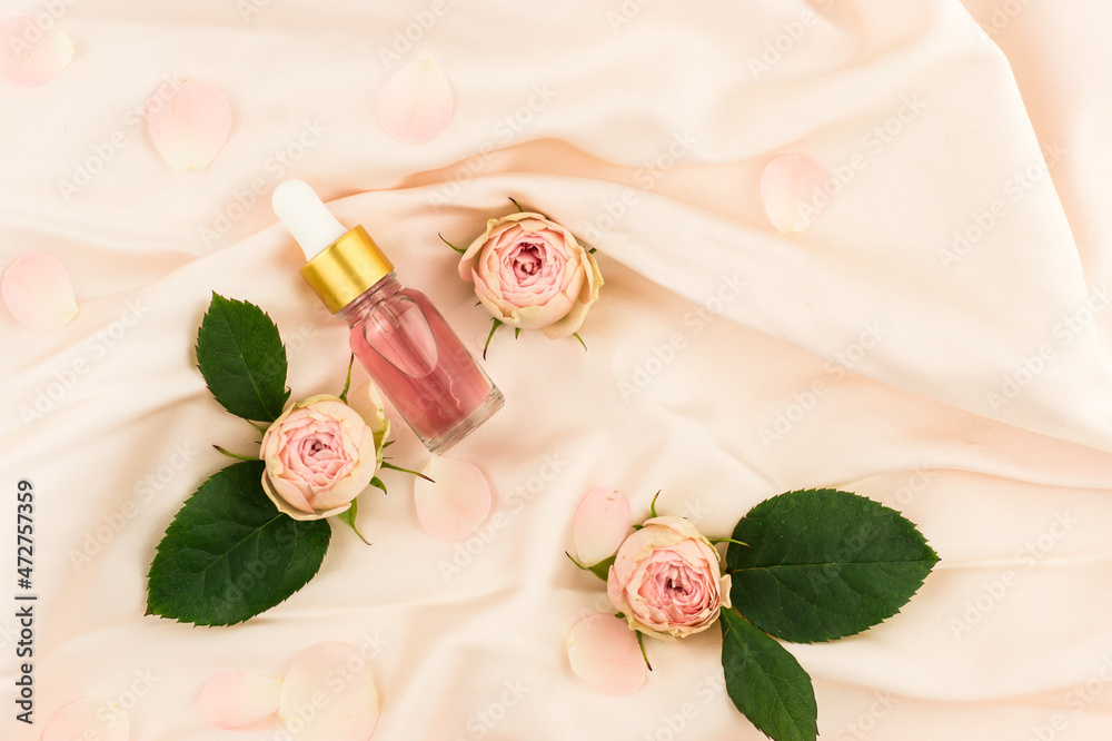 Cosmetic rose oil or essential oil in a bottle dropper on a pink textile background with rose buds and leaves. the concept of natural cosmetics. Cosmetic rose oil or essential oil in a bottle dropper on a pink textile background with rose buds and leaves. the concept of natural cosmetics.