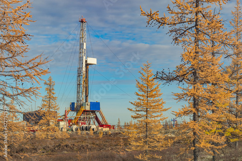 Landscape of an oil and gas field in the northern forest-tundra of Siberia. The main object is a drilling rig that blends into the picturesque autumn landscape of taiga trees