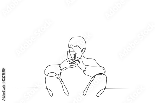 man sits leaning wall with back, apart and bent  knees holding phone with both hands - one line drawing vector