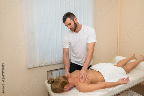 Attractive woman lying on massage bed at spa salon. Male masseur giving back massage to girl
