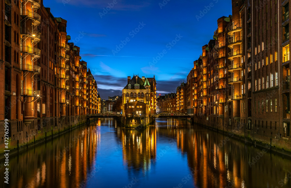 lluminated Speicherstadt with the Wasserschloss in Hamburg with reflections at the bright blue hour and blue sky - in german words: Blaue Stunde (high dynamic and detailed panoramic photography)